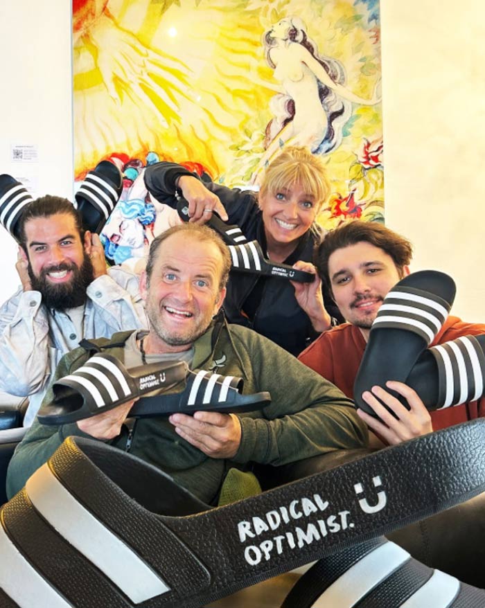 Vier Teammitglieder von Atelier Steinbüchel & Partner posieren fröhlich mit Radical-Optimist-Slidern – Social Media Moment für gelebten Optimismus
