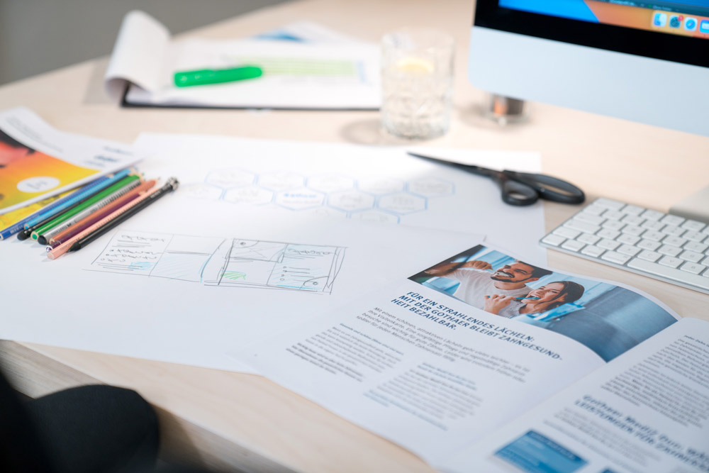 Print Design Agentur bei der kreativen Layout-Entwicklung – Skizzen, Broschüren und Designentwürfe auf einem modernen Arbeitsplatz, die professionelle Gestaltung und strategische Planung im Print zeigen.